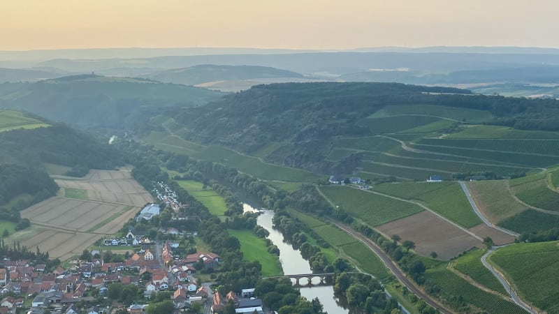 Aerial view of a river valley with a village on one side and terraced hills on the other side.