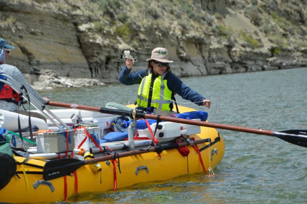 A women in a yellow raft taking a water sample from a river for the USGS.